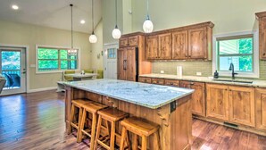 A spacious kitchen with wooden cabinets, a large island with stools, pendant lighting, and large windows.