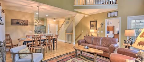 A spacious living room with a dining area, a staircase, and a loft bedroom.