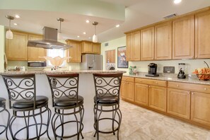 A kitchen with wooden cabinets, a stainless steel refrigerator, a microwave, and a coffee maker. There are three bar stools with metal frames. - Savannah Escape ~ 11 Mi to Historic District! (Savannah)