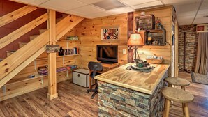 A cozy cabin interior with a wooden staircase, a TV, a stone bar area, and a bookshelf. - Hot Tub & Deck! High Country Cabin Near Blue Ridge (Mineral Bluff)