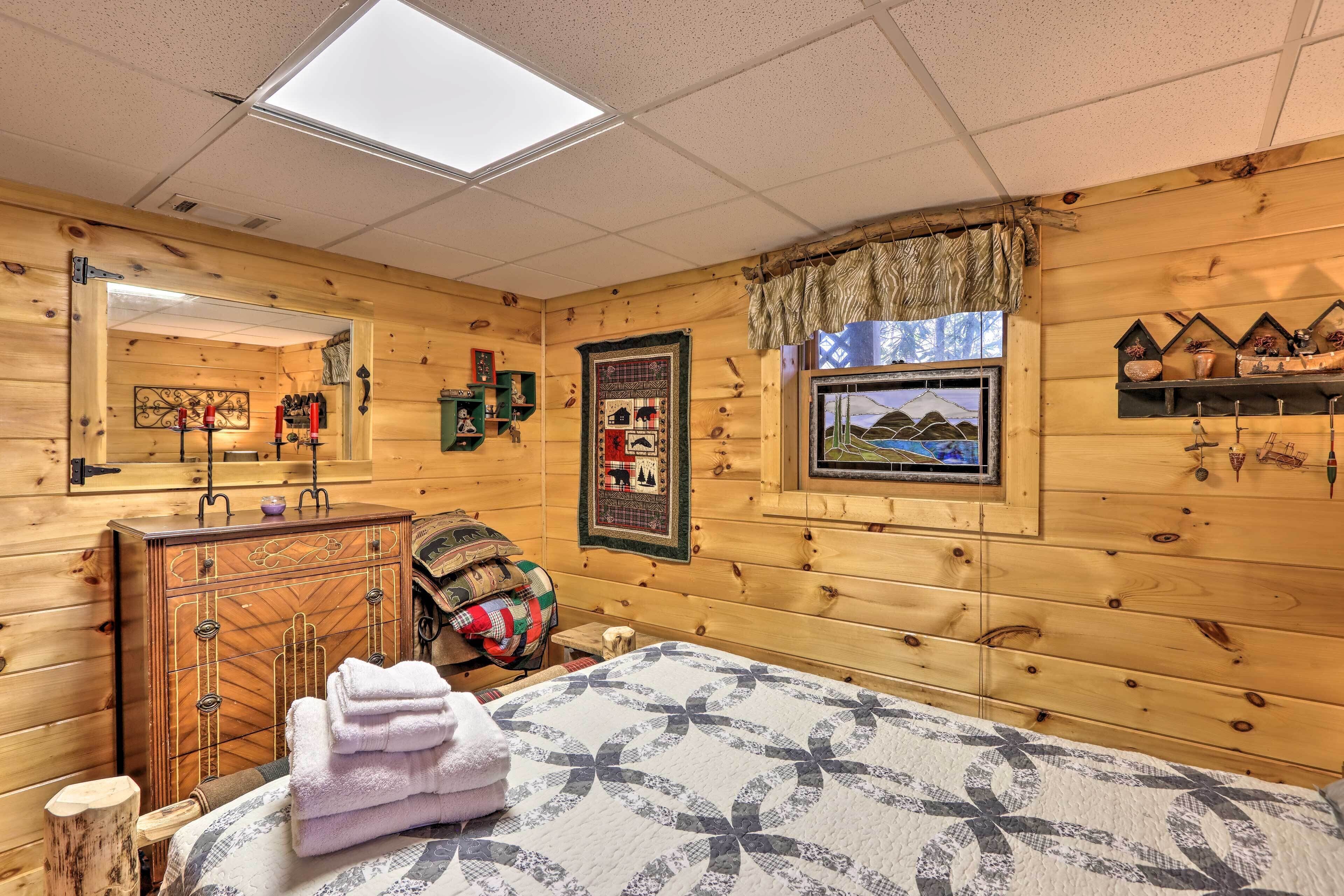 A cozy wooden room with a bed, a dresser, a window with a view, and a shelf with decorative items.