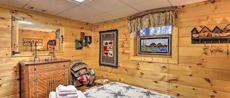 A cozy wooden room with a bed, a dresser, a window with a view, and a shelf with decorative items.