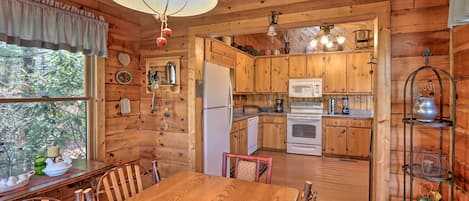 A wooden cabin interior with a dining area, kitchen, and a large window.