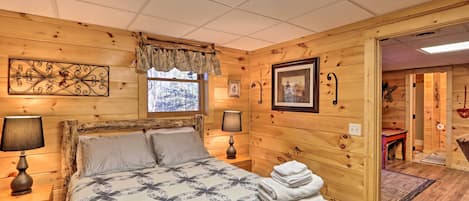 Une chambre confortable, aménagée dans un chalet en bois, avec un lit, deux lampes de chevet, une fenêtre donnant sur un paysage agréable et une porte menant à une autre pièce.