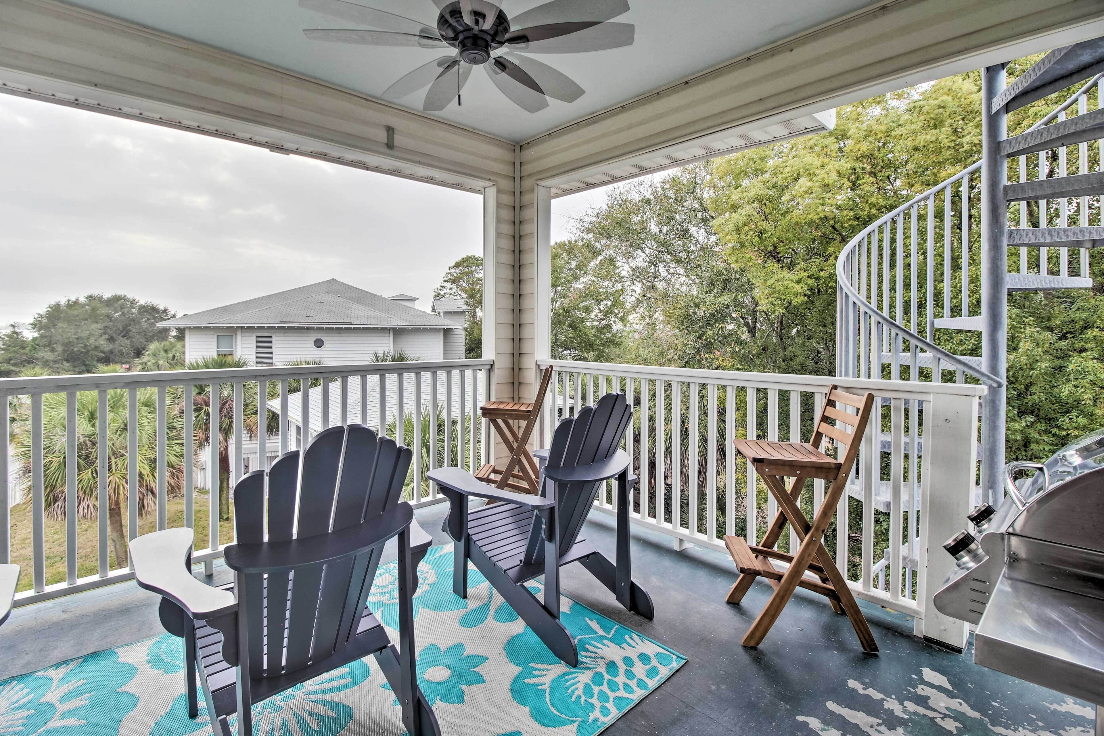 A covered porch with Adirondack chairs, a grill, and a spiral staircase.
