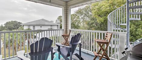 A covered porch with Adirondack chairs, a grill, and a spiral staircase.
