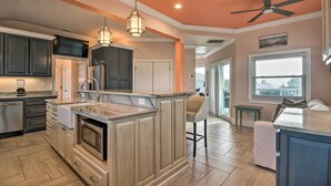 A spacious kitchen with dark cabinets, a marble island, and a ceiling fan.