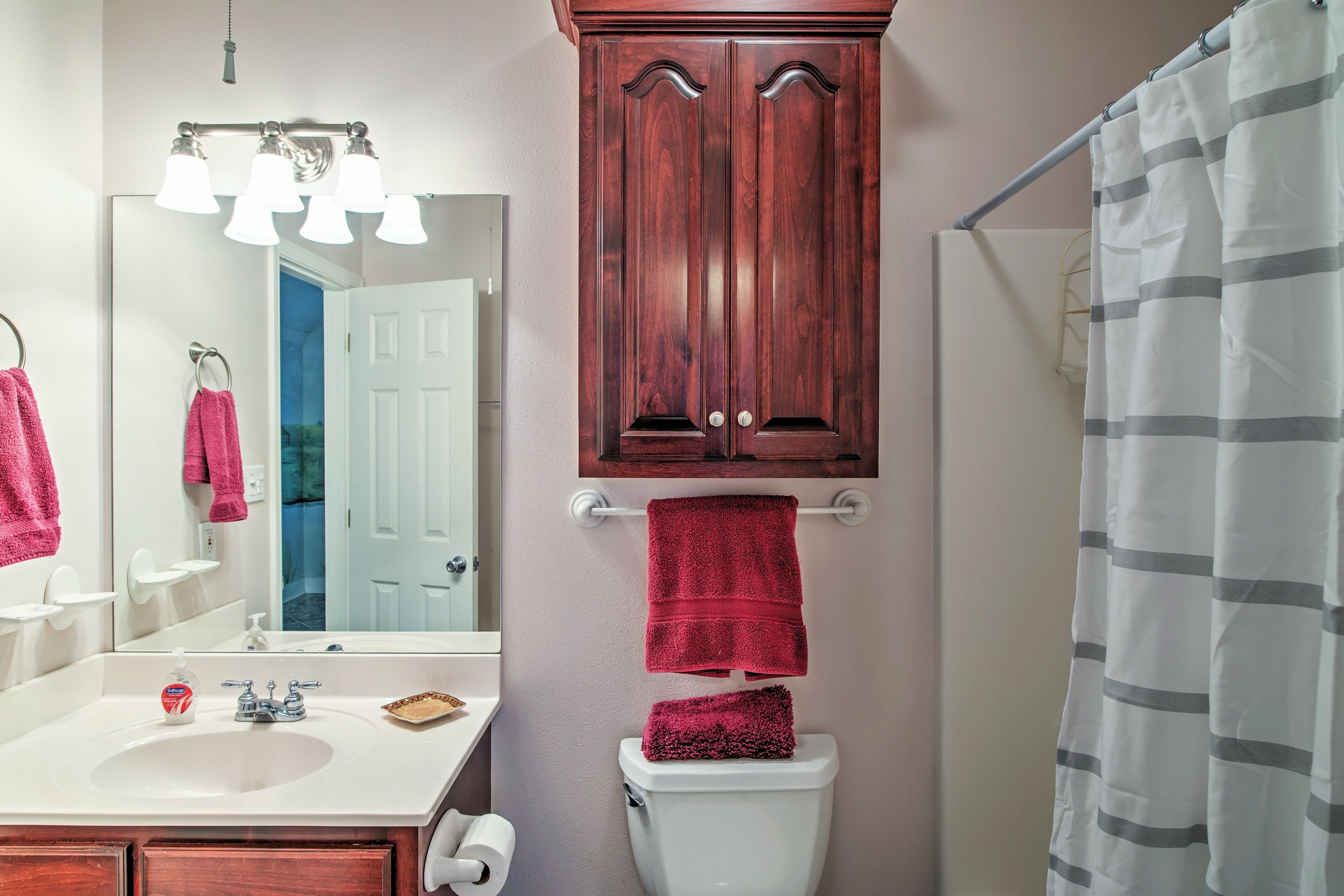 A bathroom with a white sink, a mirror, a wooden cabinet above the toilet, and a striped shower curtain.