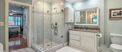 A bathroom with a glass-enclosed shower, white cabinetry, a marble-tiled floor, and a white toilet.