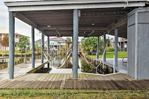 Une jetée en bois, surmontée d’une promenade couverte qui surplombe l’eau et soutenue par des piliers, mène à un bâtiment doté d’un balcon.