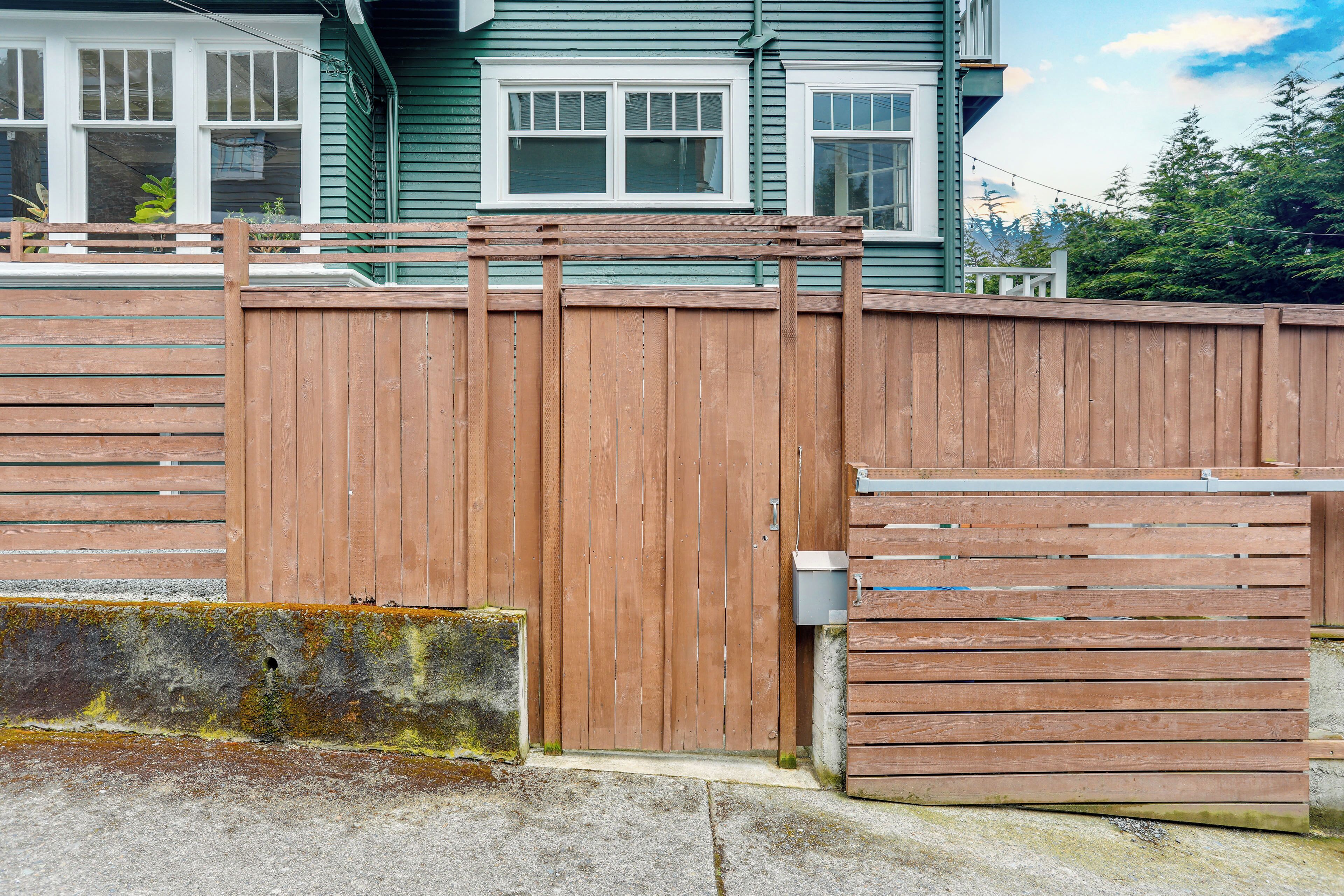 A wooden fence with a gate, a concrete base, and a house with green siding and white trim in the background.