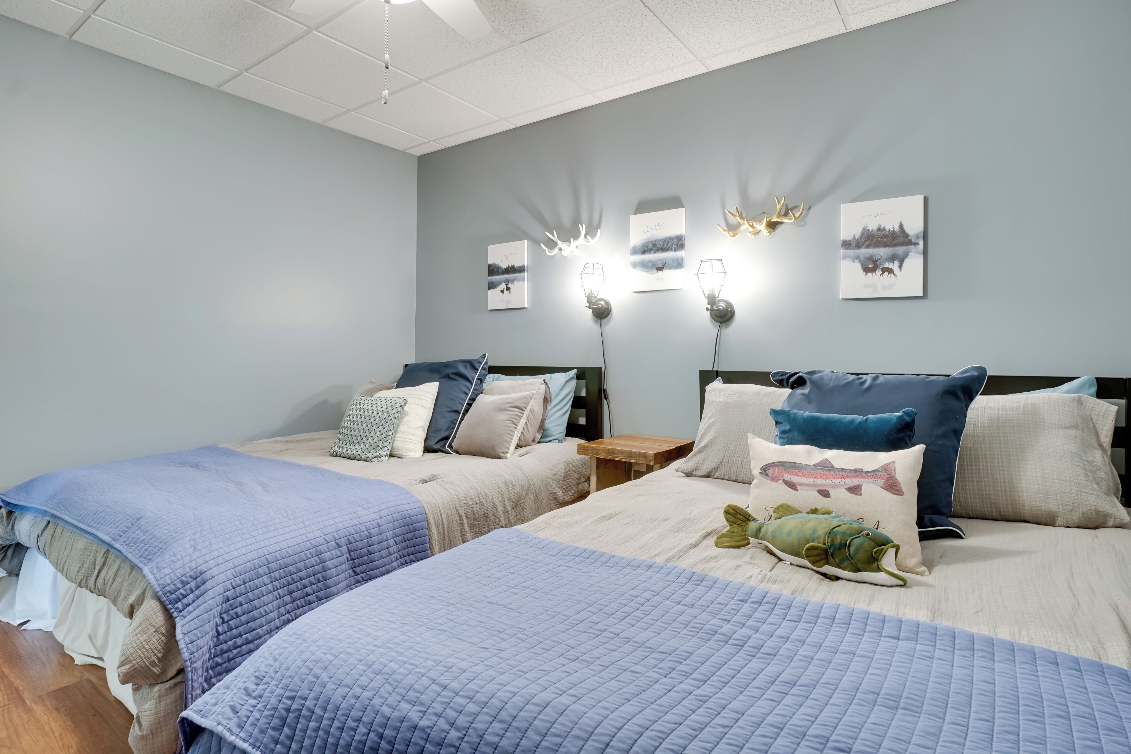 Un dormitorio con dos camas, cada una con una colcha azul acolchada, varias almohadas y luces fijadas a la pared.