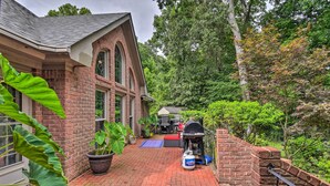 A brick house with a patio, a barbecue grill, and a large potted plant.