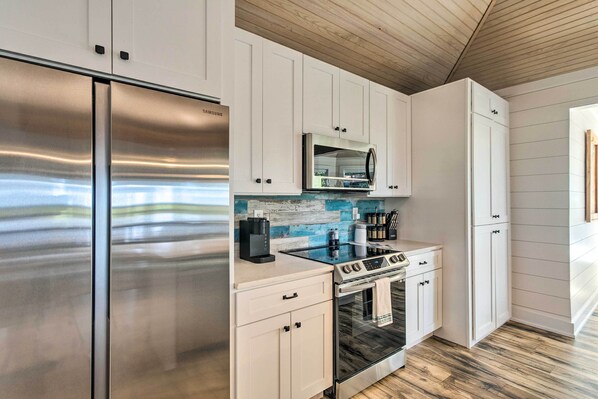 Una cocina moderna con electrodomésticos de acero inoxidable, muebles de cocina blancos y techo de madera.
