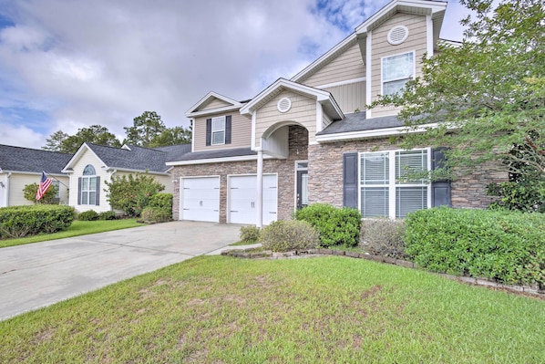 A two-story house with a stone facade, a front garage, and a well-maintained lawn.