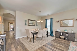 A dining area with a table and chairs, a chandelier, a console table with decorative items, and a patterned rug.