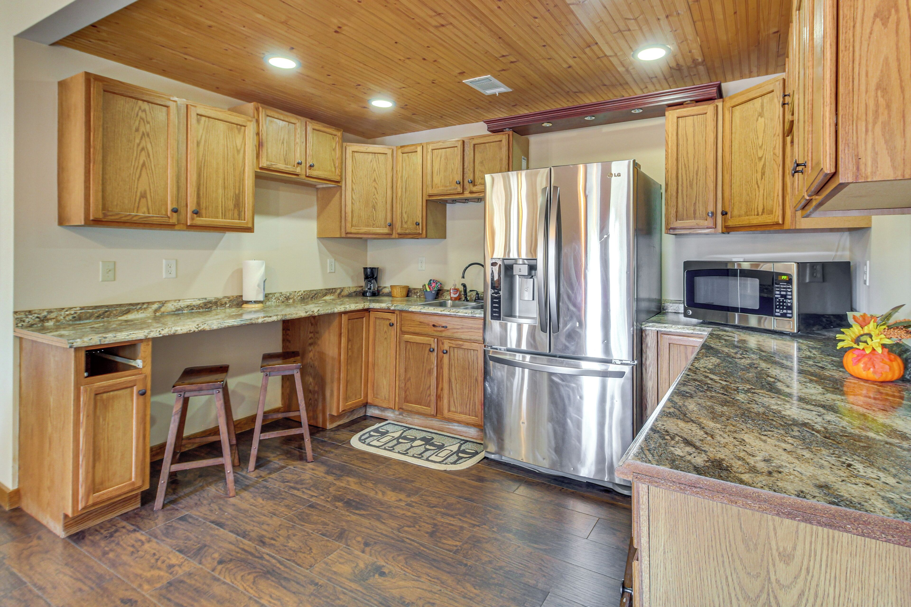 A kitchen with wooden cabinets, a stainless steel refrigerator, a microwave, and a granite countertop.