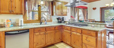 A kitchen with wooden cabinets, a dishwasher, a window with curtains, and a stove.