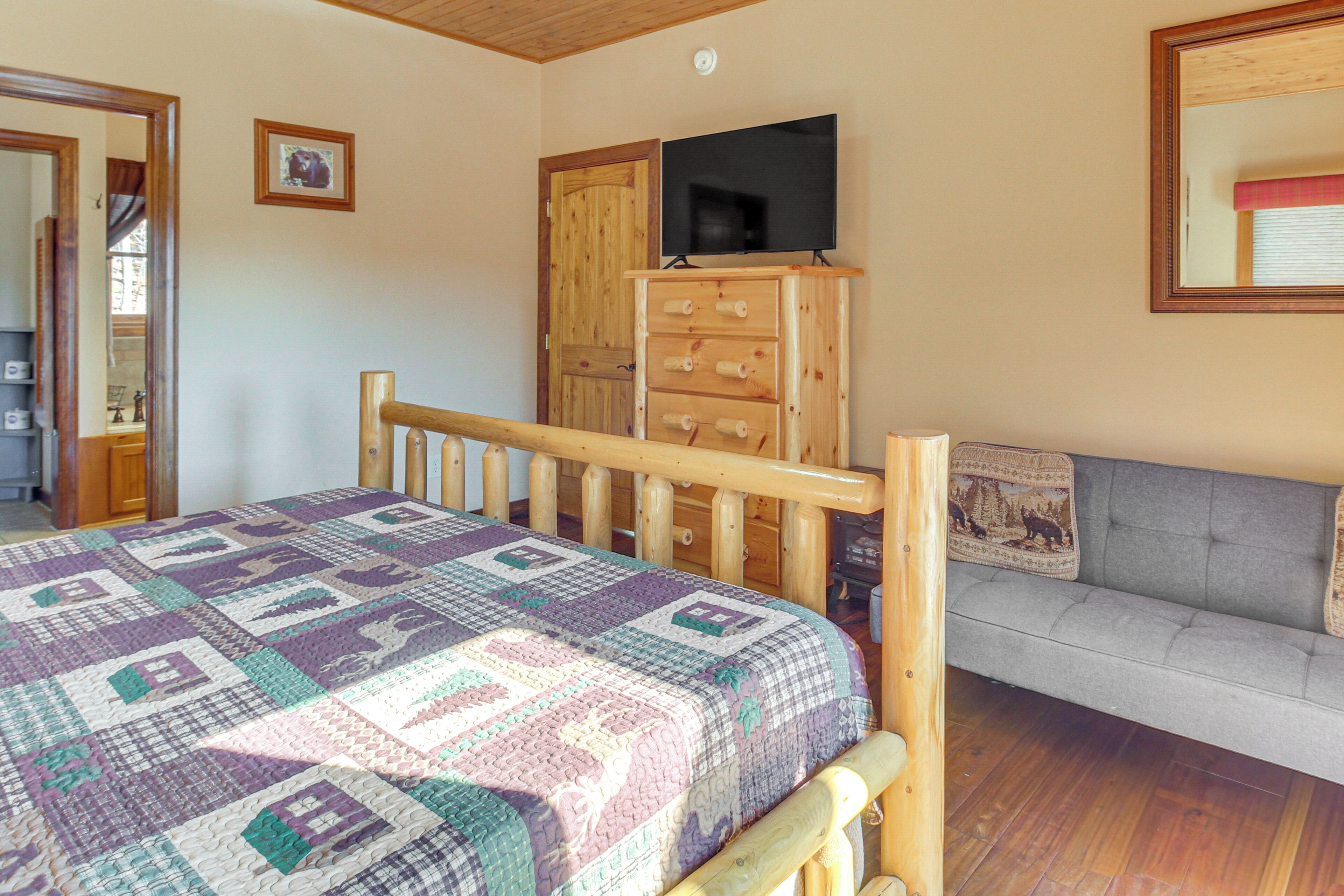 Ein Schlafzimmer mit einem Holzbett, einer Couch, einem Fernseher auf einer Holzkommode und einer gesteppten Decke auf dem Bett.