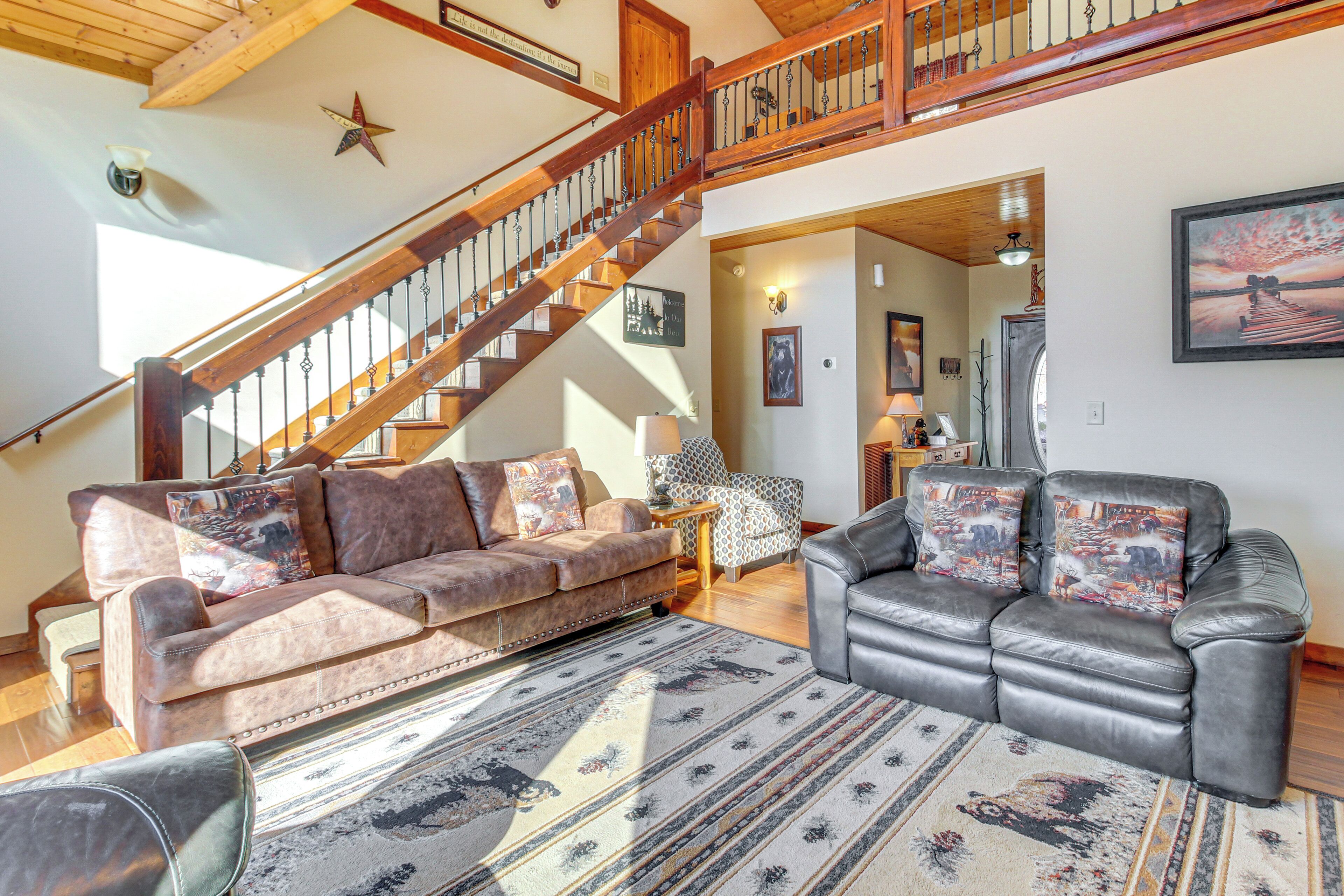 Un vaste espace de vie agrémenté d’un escalier en bois, de canapés en cuir et d’un grand tapis.