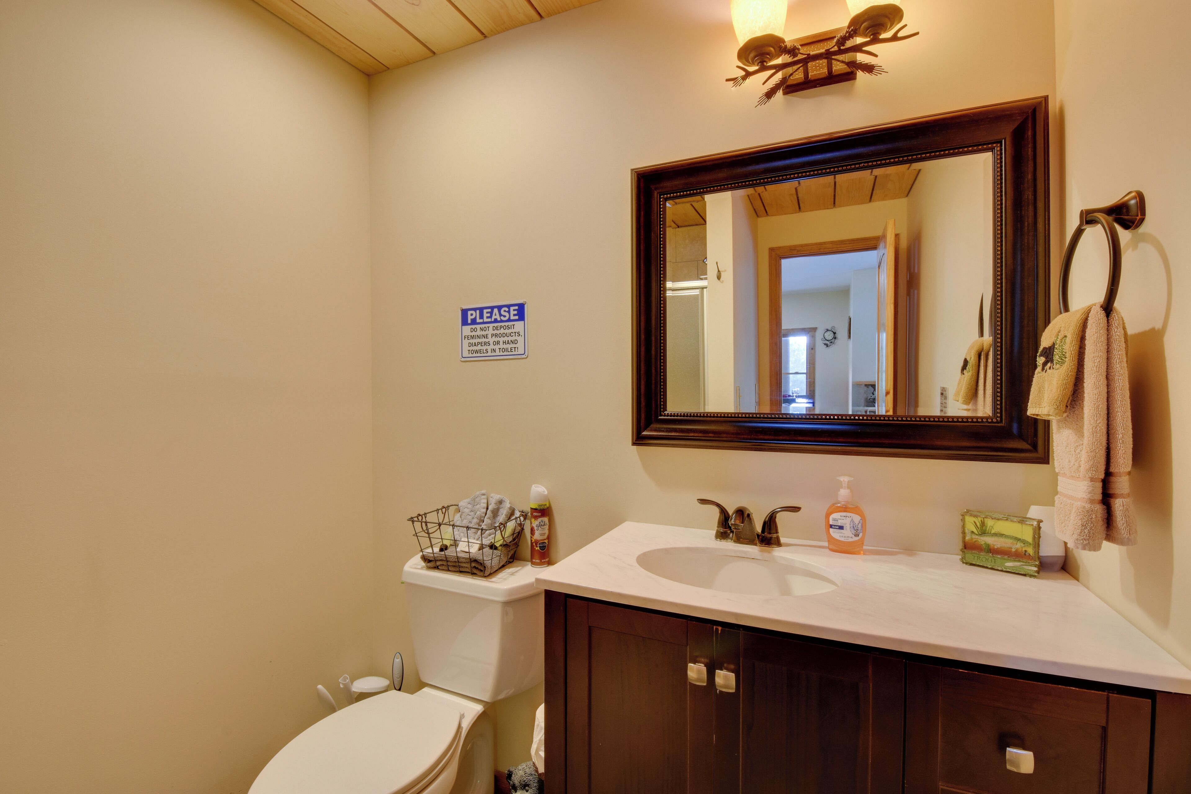 A bathroom with a sink, mirror, and a sign instructing not to deposit items in the toilet.