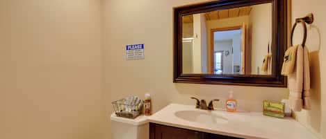 A bathroom with a sink, mirror, and a sign instructing not to deposit items in the toilet.
