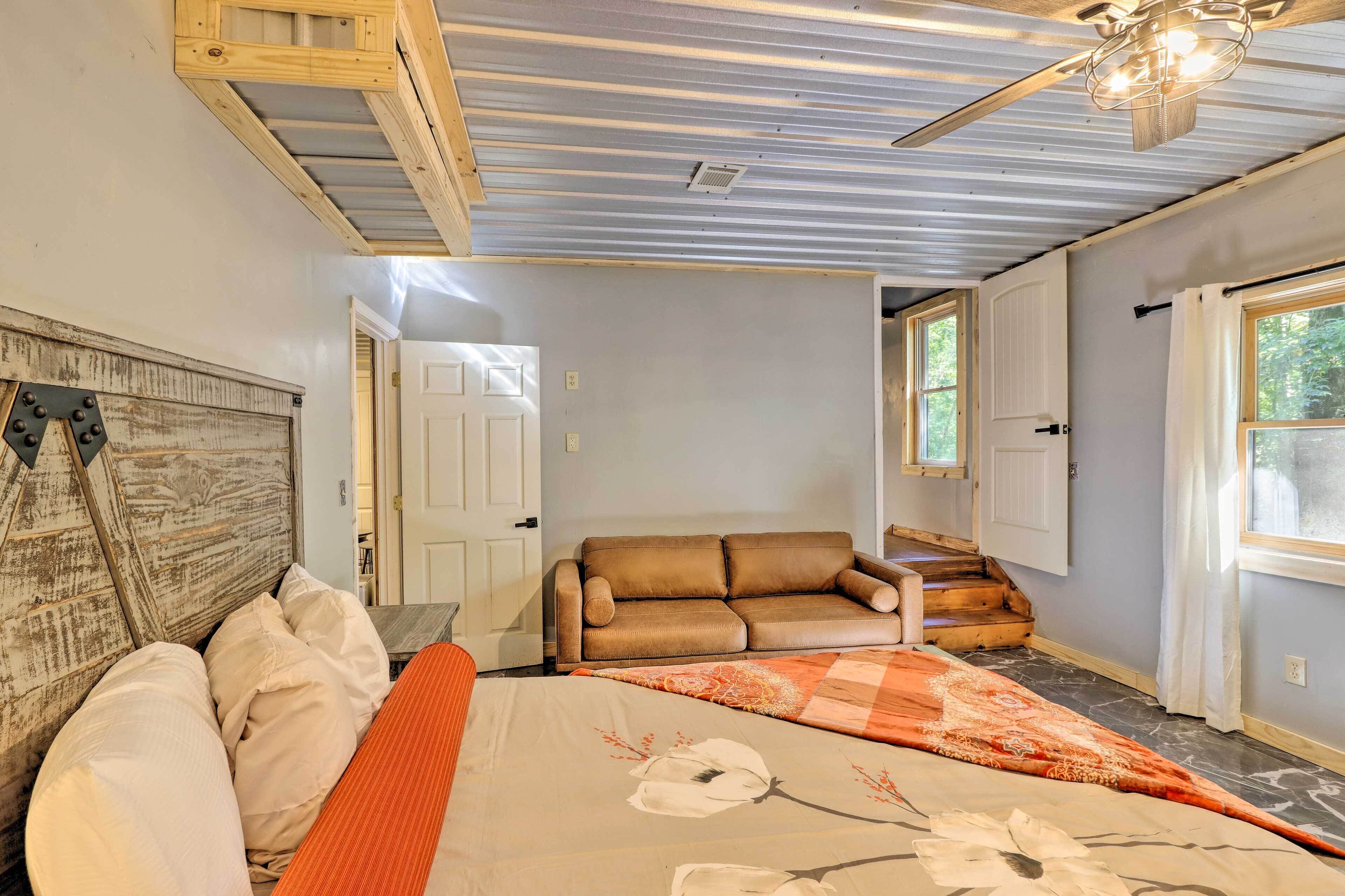 A bedroom with a bed, a wooden headboard, a brown leather sofa, a window, and a ceiling fan.