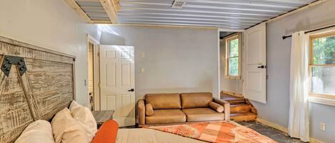 A bedroom with a bed, a wooden headboard, a brown leather sofa, a window, and a ceiling fan.