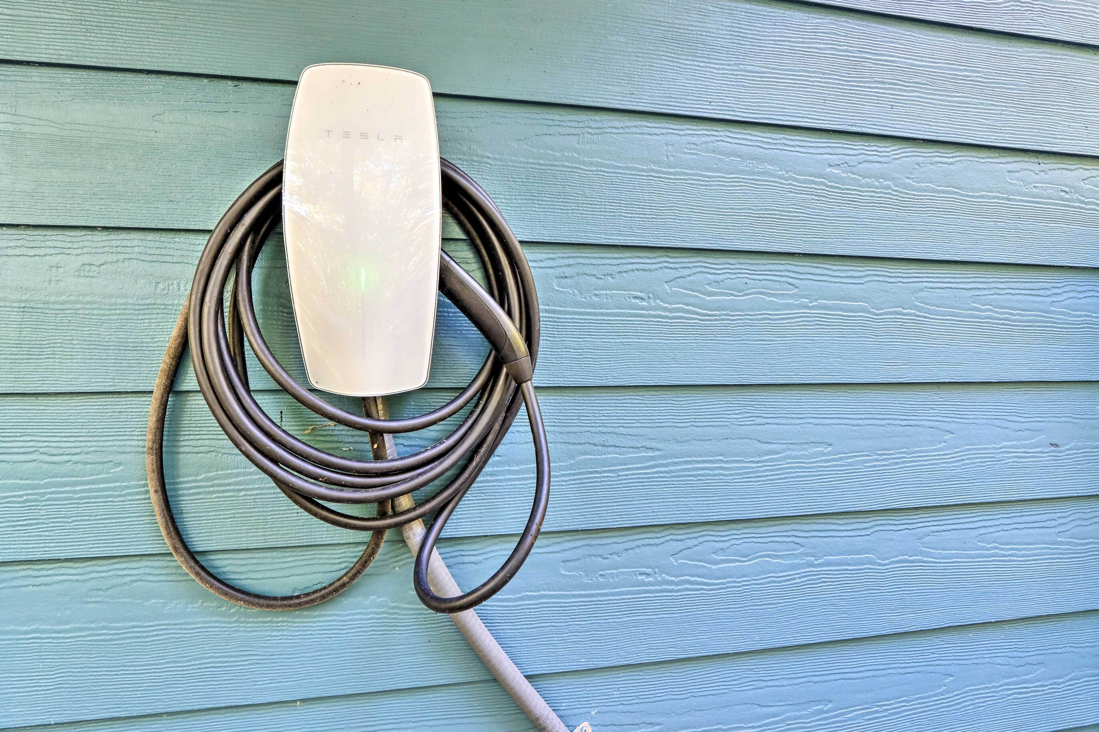 A Tesla charging station mounted on a light blue wooden wall.