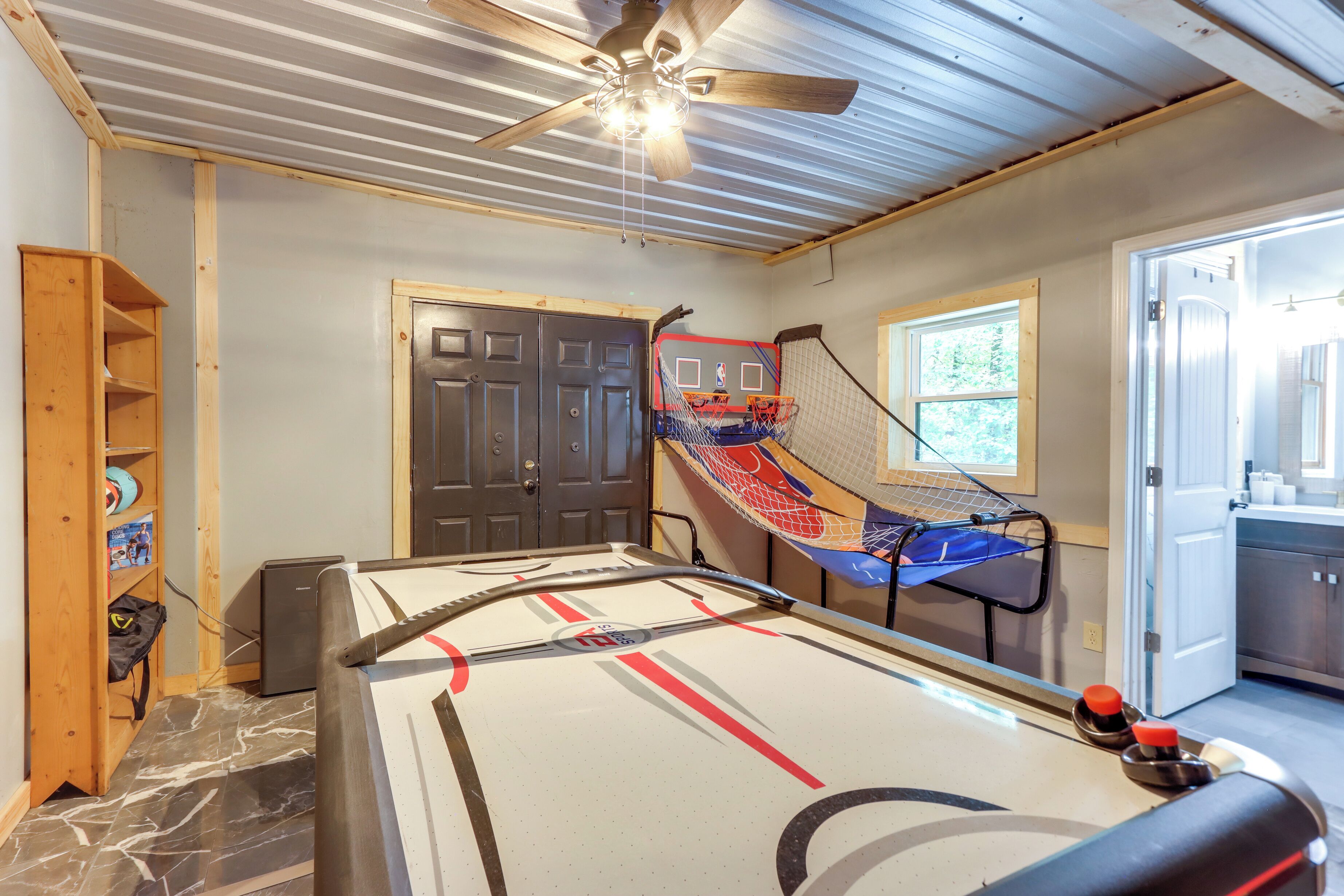 A room with a pool table, a ceiling fan, and a door leading to another room.