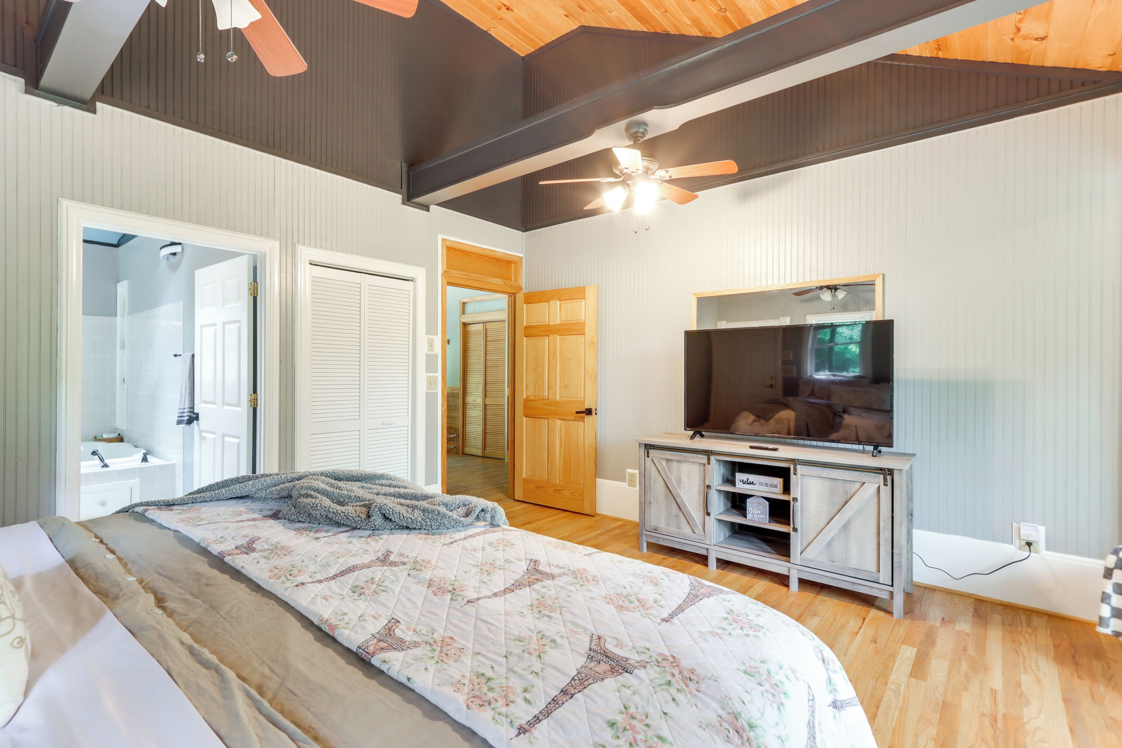 A bedroom with a bed, a TV, a ceiling fan, and a wardrobe.