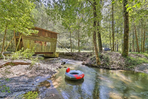 A rustic wooden cabin by a forest stream with a raft.
