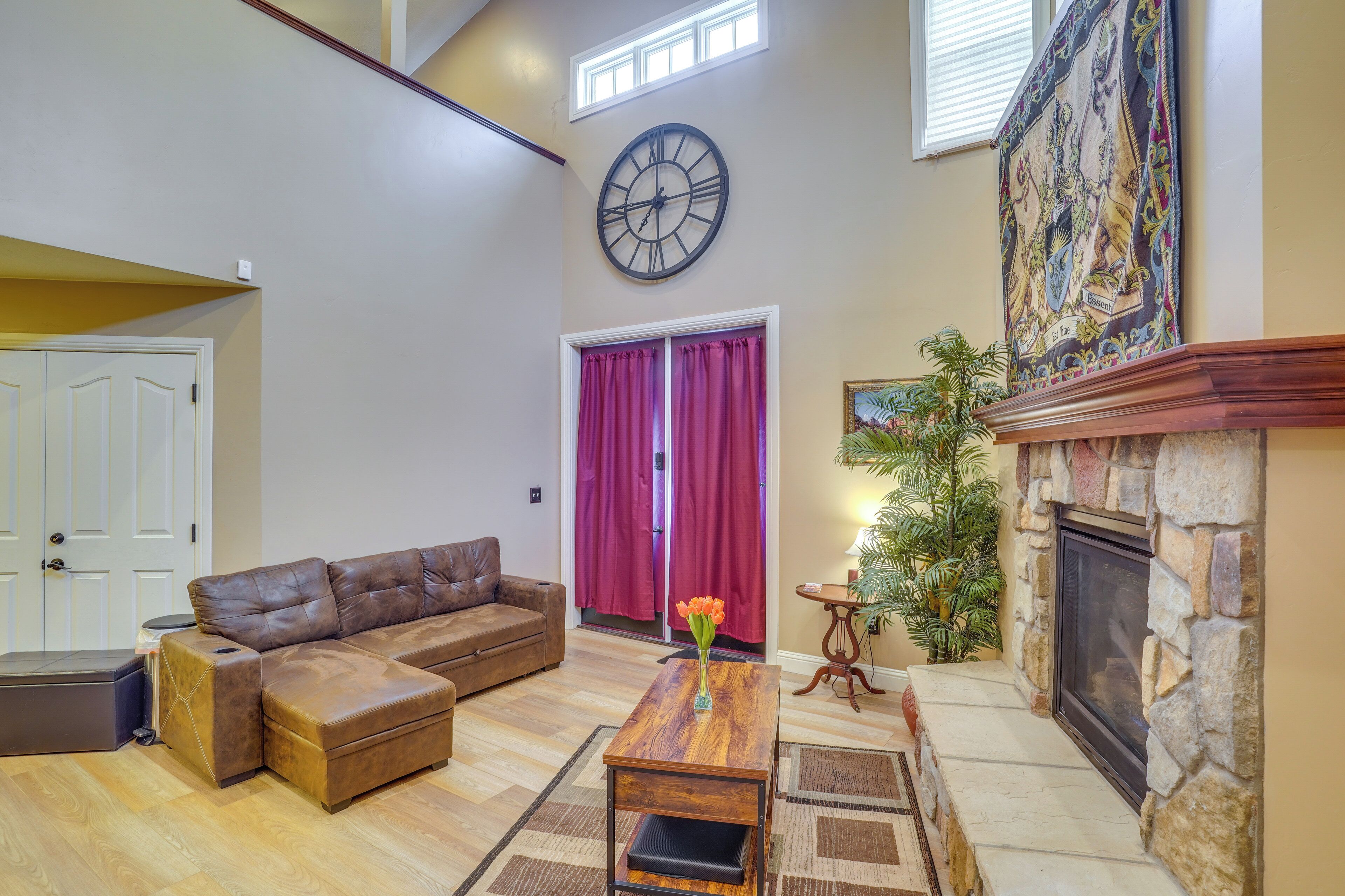 A spacious living room with a brown leather sectional sofa, a wooden coffee table, a fireplace, and a large wall clock.