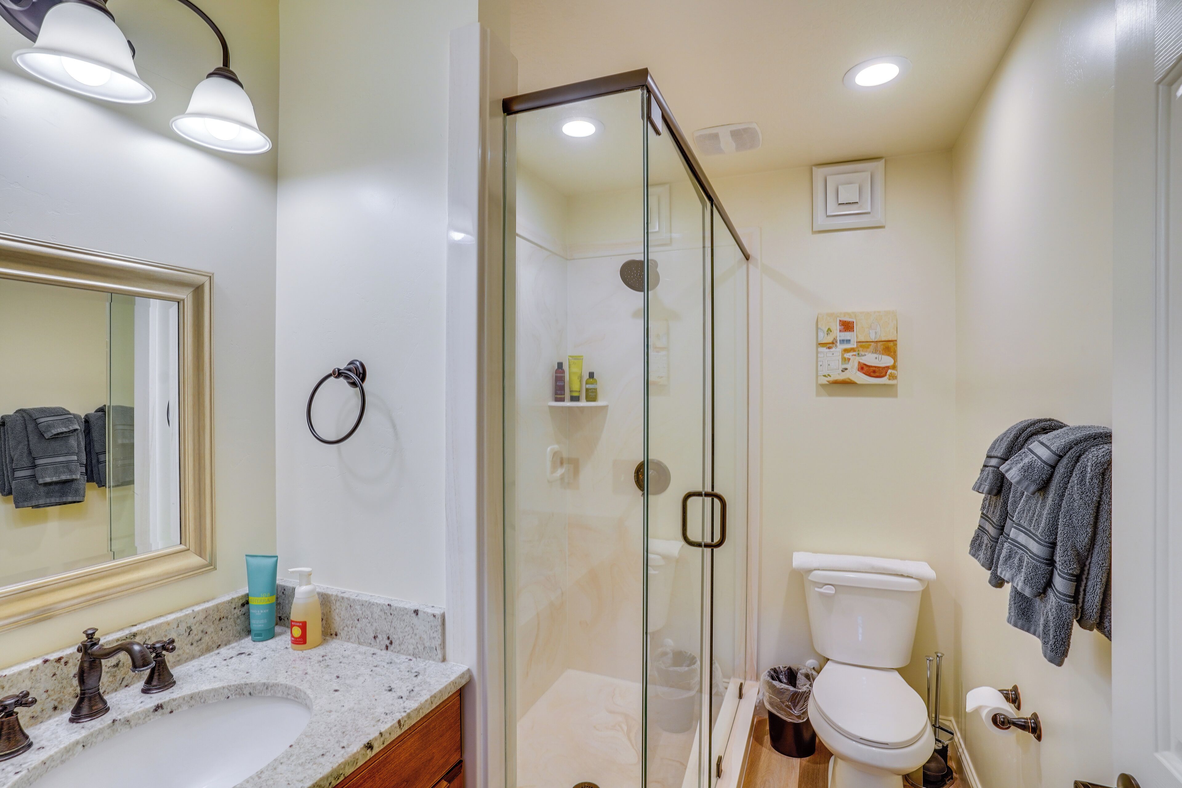 Un baño con ducha envuelta en vidrio, un lavabo con encimera de mármol, un inodoro y un espejo con toallero.