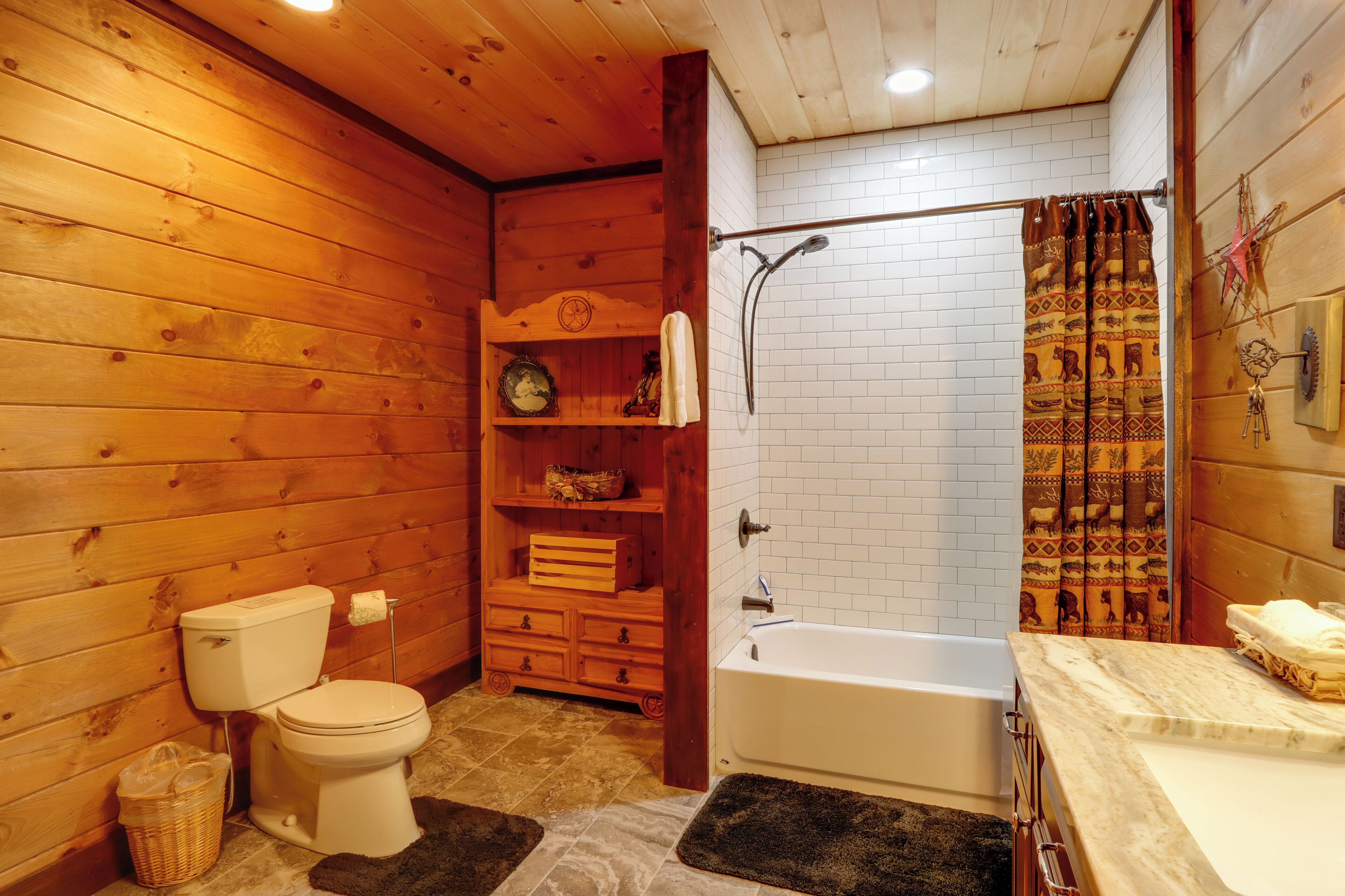 Baño de cabaña de madera con inodoro, ducha y repisa de madera con artículos de aseo.