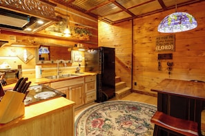 A wooden cabin kitchen with a refrigerator, stove, sink, and wooden cabinets.