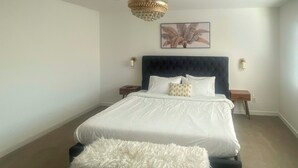 Een slaapkamer met een groot bed, een zachte witte bank, een donkerblauwe hoofdeinde en een kroonluchter.