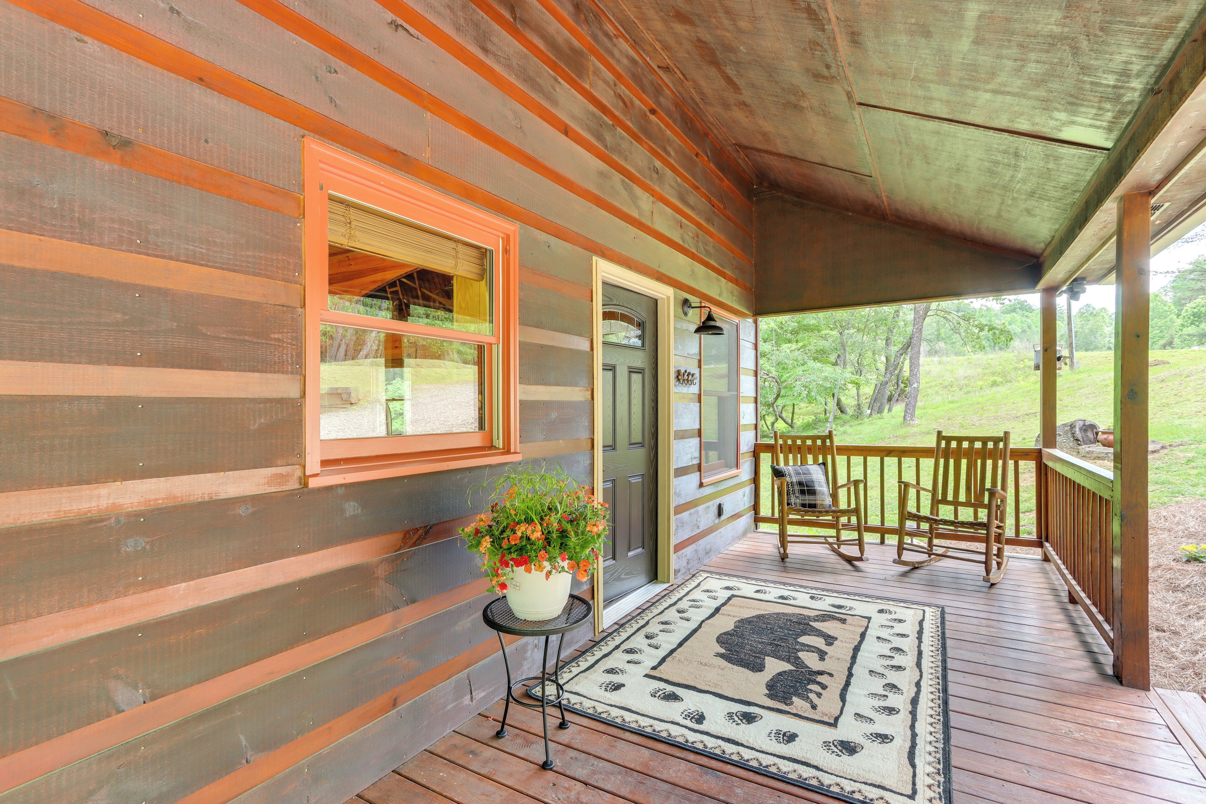 A wooden cabin with a porch, a potted plant, and a rug with a bear design.