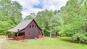 Un chalet rustique doté d’une véranda, entouré d’une végétation luxuriante et d’arbres.