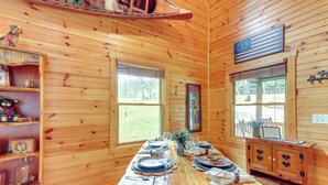 L’intérieur d’un chalet en bois comprend une table à manger pour quatre personnes, un buffet en bois orné de découpes en forme de cœur et un drapeau accroché au mur.