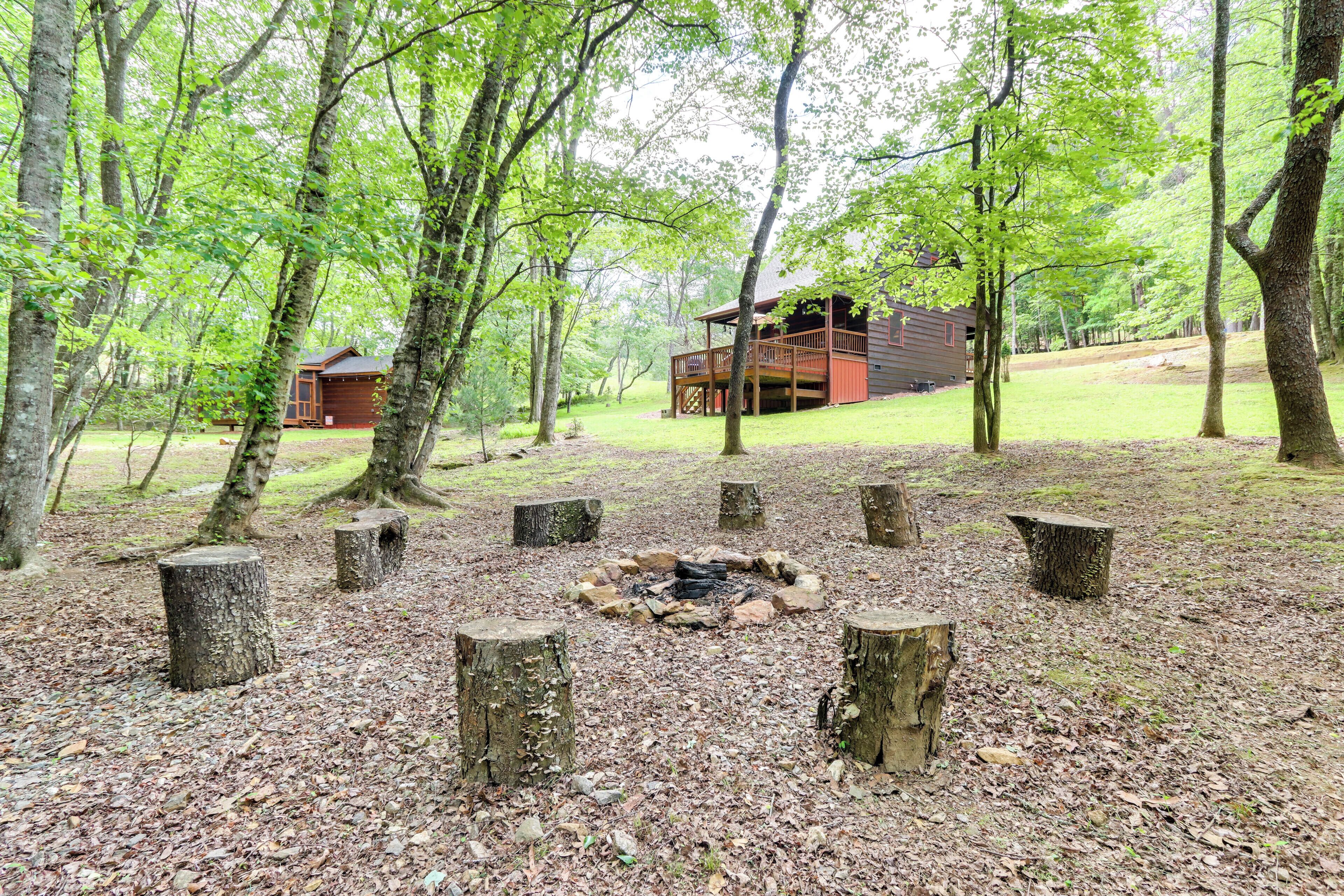 A cabin surrounded by trees, a fire pit, and a wooden deck.