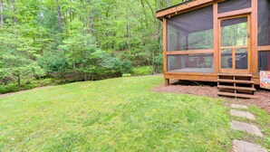 Une cabane en bois dotée d’une véranda grillagée, entourée d’une forêt luxuriante.