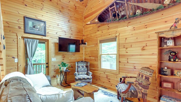 L’intérieur chaleureux d’un chalet en bois comprend un canapé, un fauteuil et un téléviseur à écran plat fixé au mur.