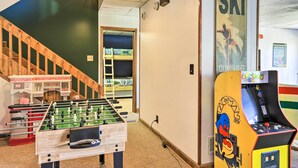 A room with a foosball table, a pinball machine, and a staircase leading to a bunk bed area. - Lakefront Macon Getaway w/ Stunning Boathouse (Macon)
