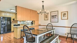 A modern kitchen with wooden cabinets, a stainless steel refrigerator, a dining table with chairs, and a chandelier. - Lakefront Macon Getaway w/ Stunning Boathouse (Macon)