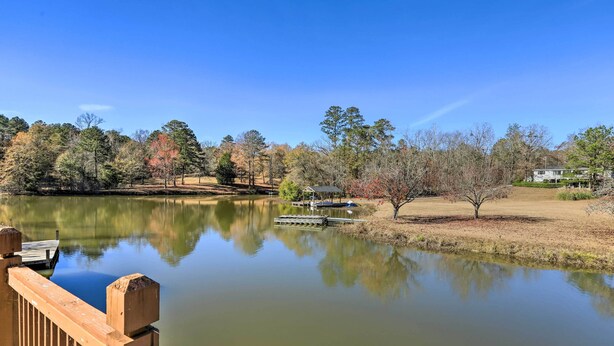 A calm lake with a wooden dock, surrounded by trees and a house in the background. - Lakefront Macon Getaway w/ Stunning Boathouse (Macon)