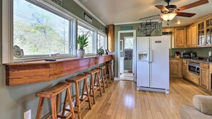 A kitchen with wooden bar stools, a white refrigerator, wooden cabinets, and a ceiling fan. - Cozy Creekside Cabin w/ Grill: Fish & Explore! (Thomaston)