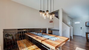 A spacious kitchen with a long wooden table, hanging pendant lights, and a staircase leading to an upper level. - Loveland Home w/ Private Hot Tub + Wood Fireplace! (Loveland)