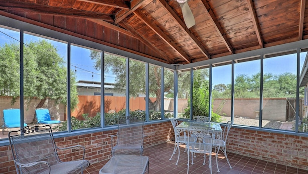 A covered patio with metal chairs and a table, large windows, and a brick wall. - Pet-friendly Home, 4 Miles to U of A Campus (Tucson)