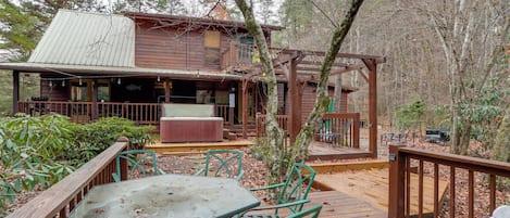 A wooden cabin with a deck, outdoor seating, and a hot tub.